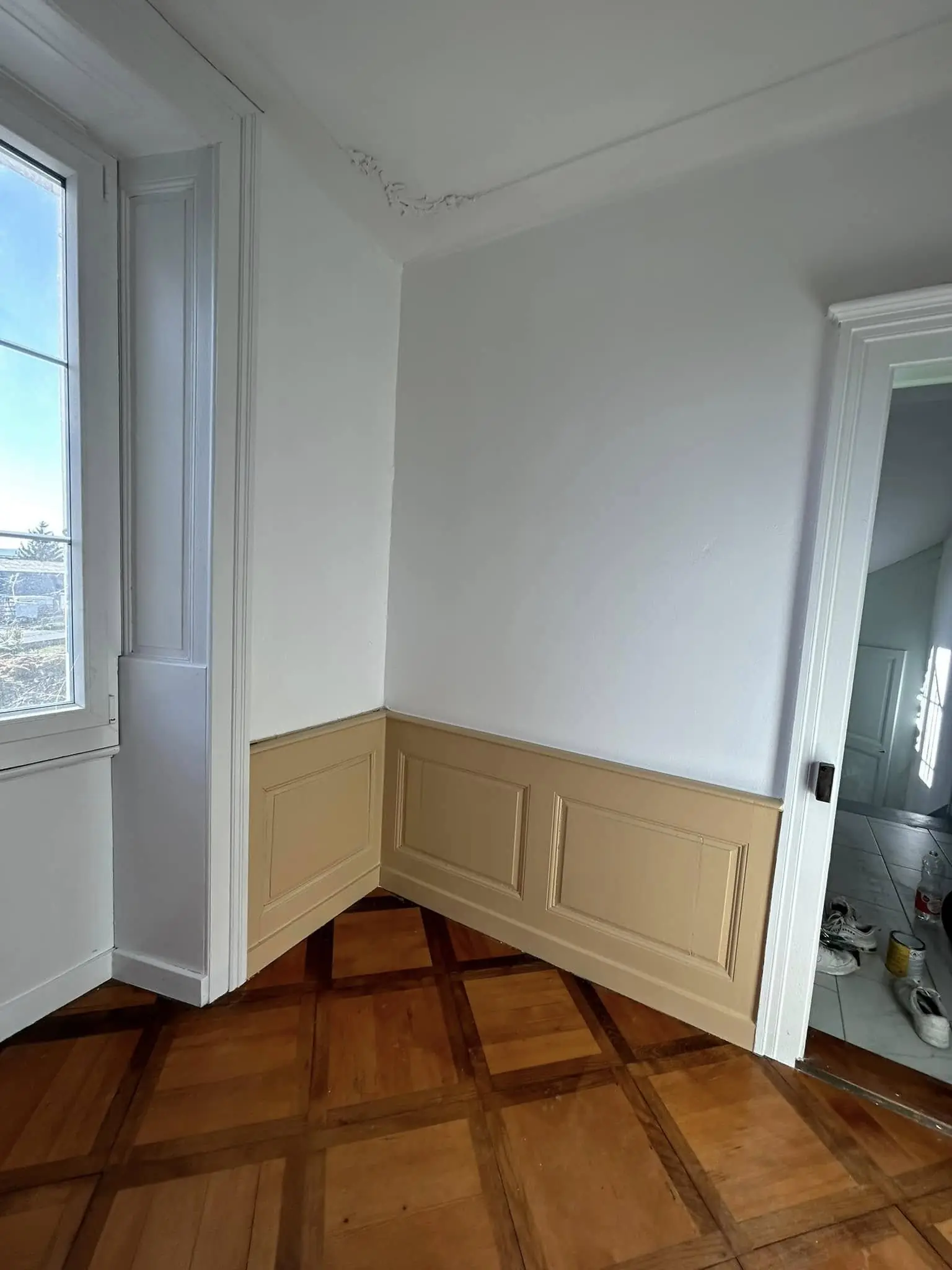Séjour vide avec soubassement beige et parquet en point de Hongrie