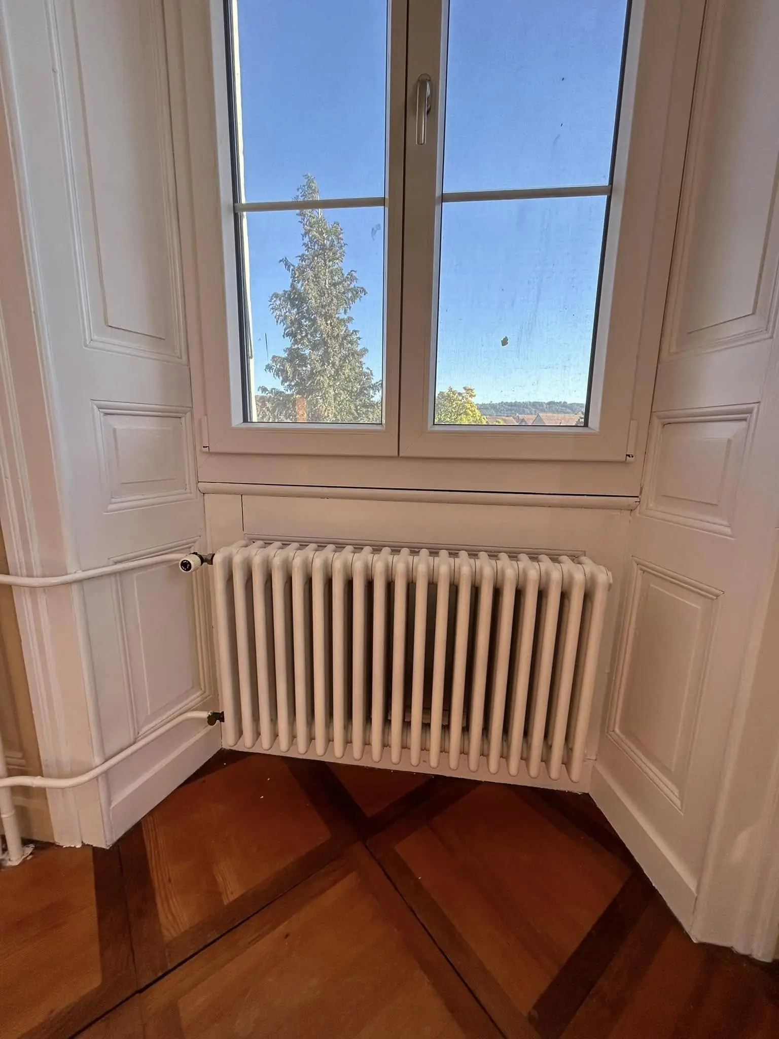 Fenêtres d'angle et radiateur à colonnes devant un soubassement beige
