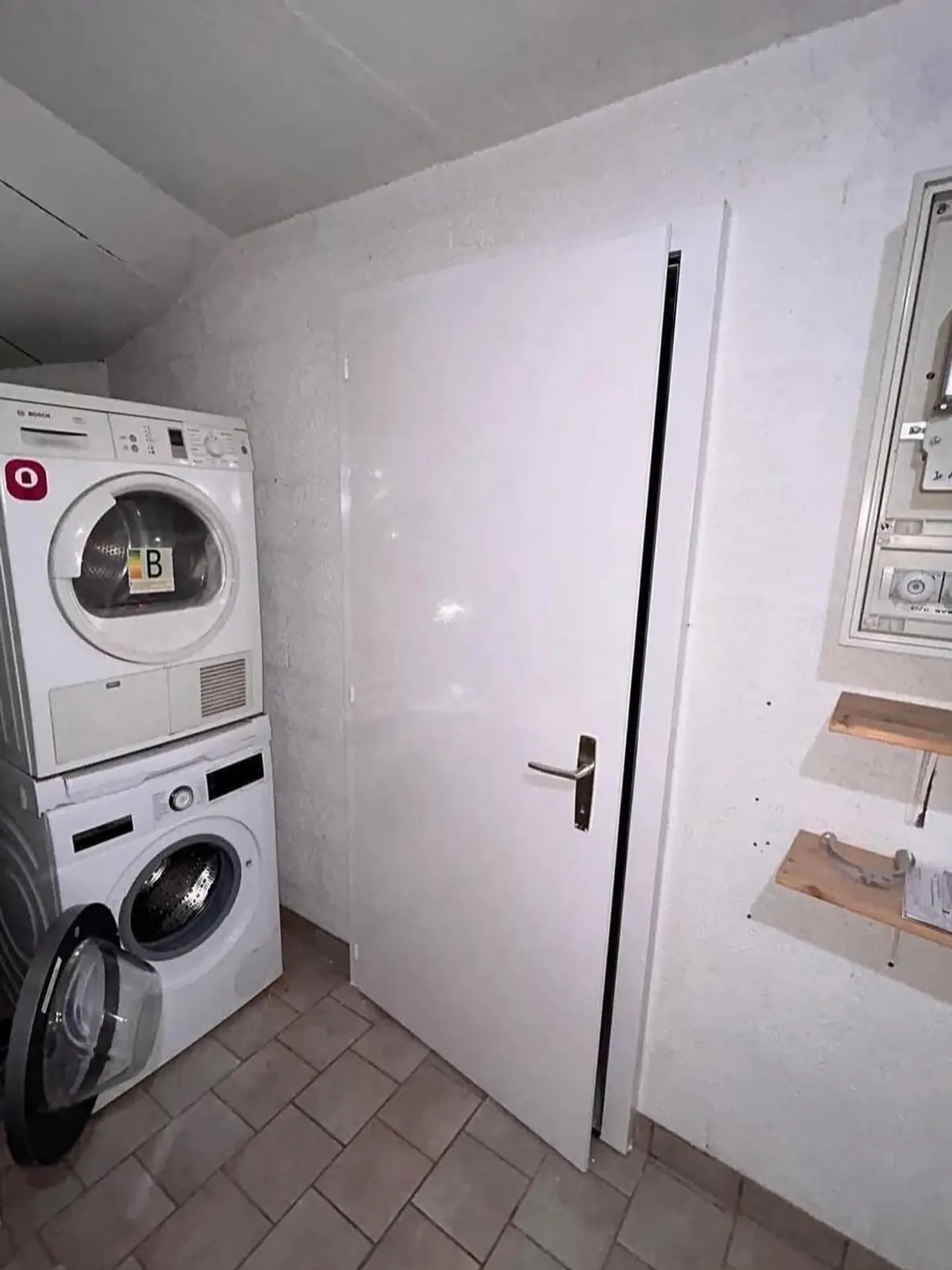 Buanderie repeinte en blanc avec porte et tableau électrique